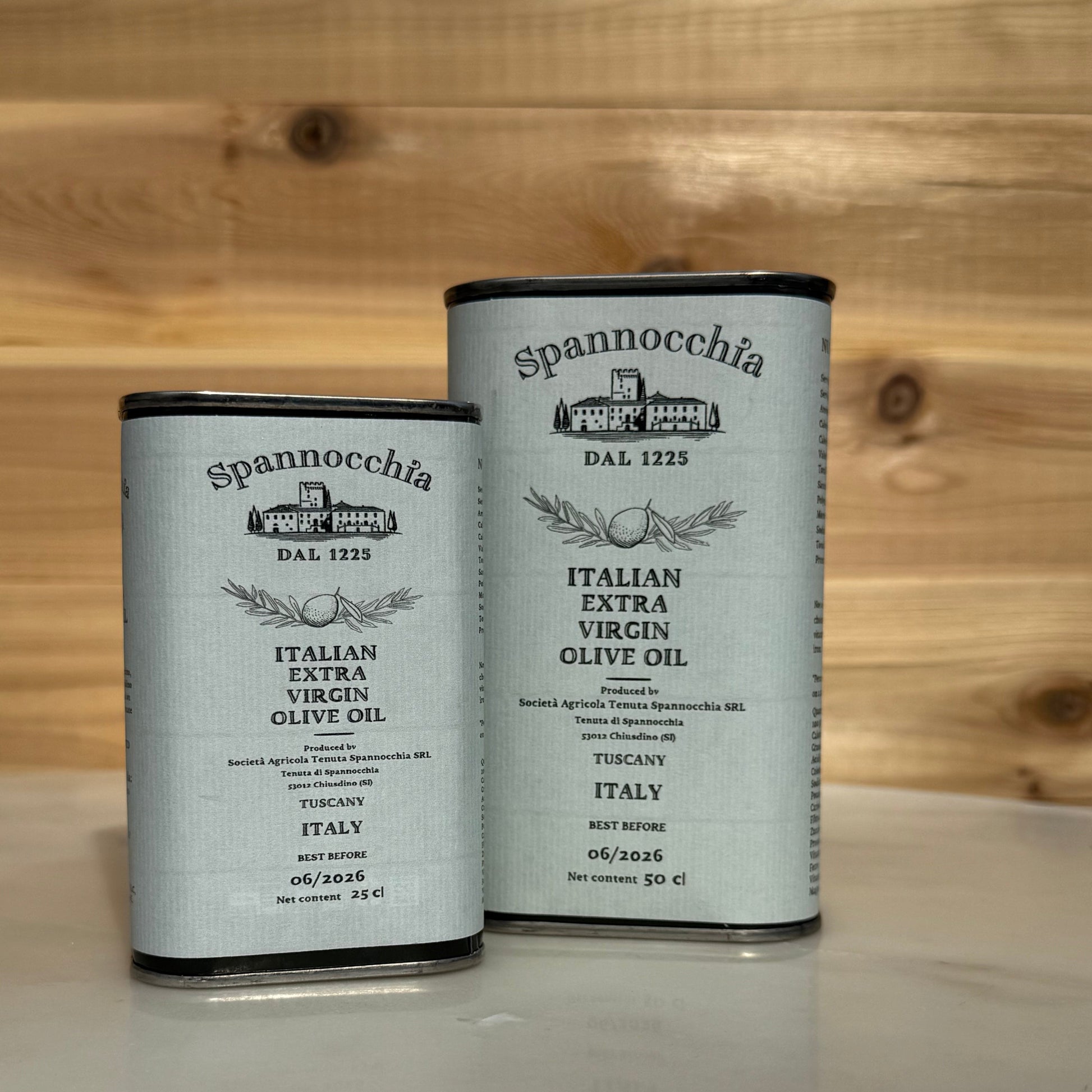 One large and one small can of olive oil. They are on a white marble surface with a wood background out of focus.