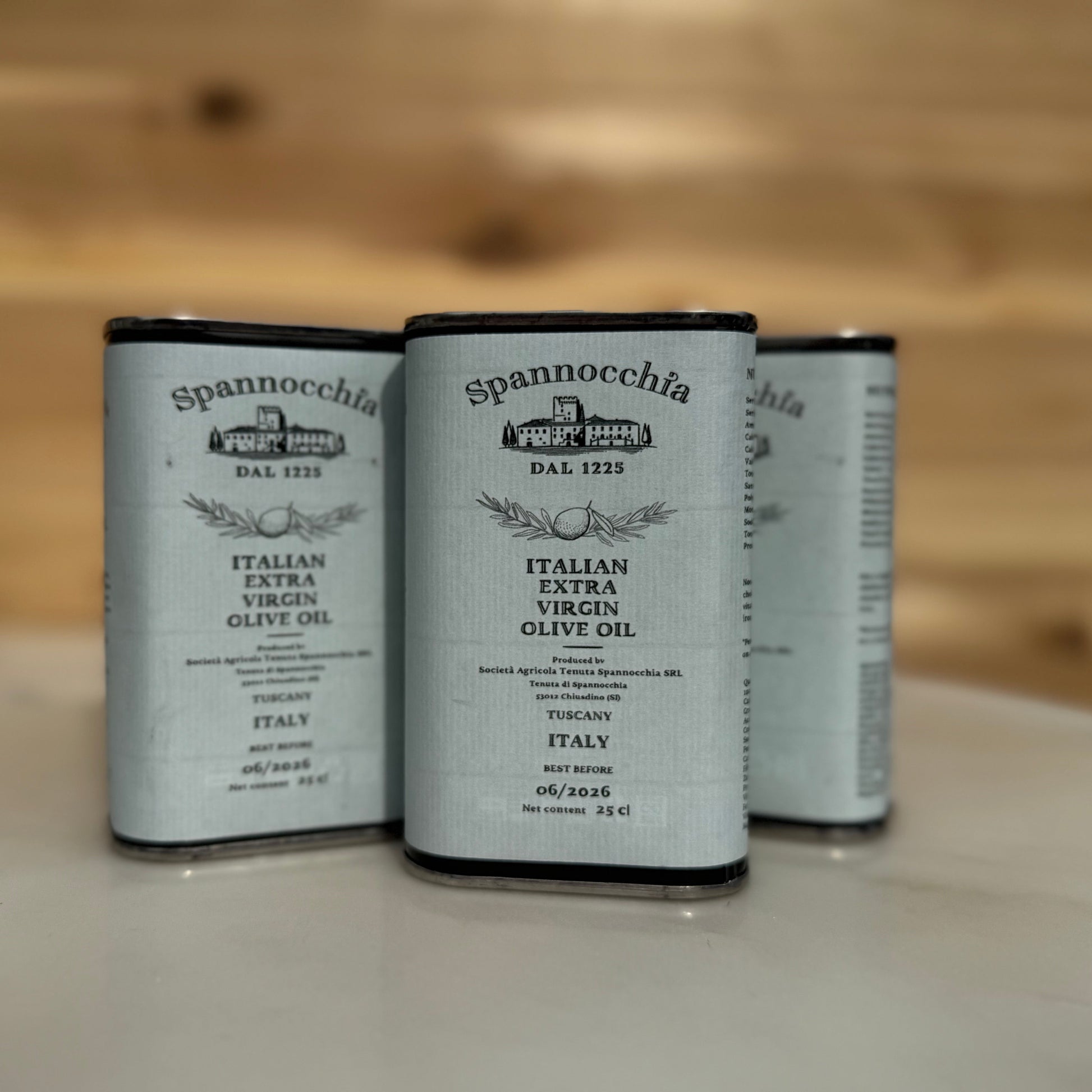 Three 250ml cans of olive oil. They are on a white marble surface with a wood background out of focus.