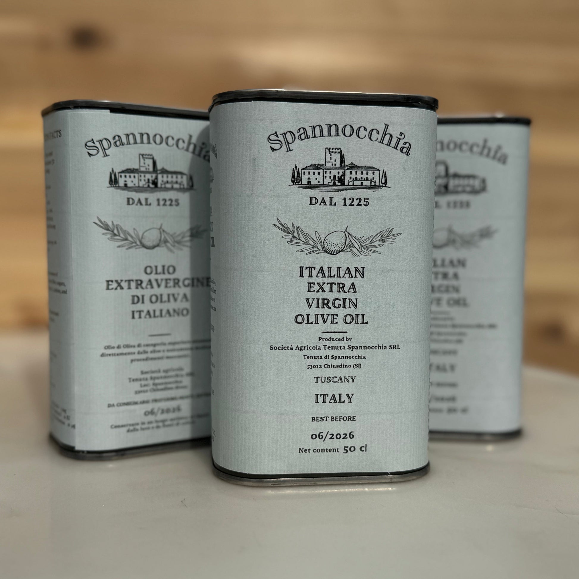 Three 500ml cans of olive oil with one in front. They are on a white marble surface with a wood background out of focus.