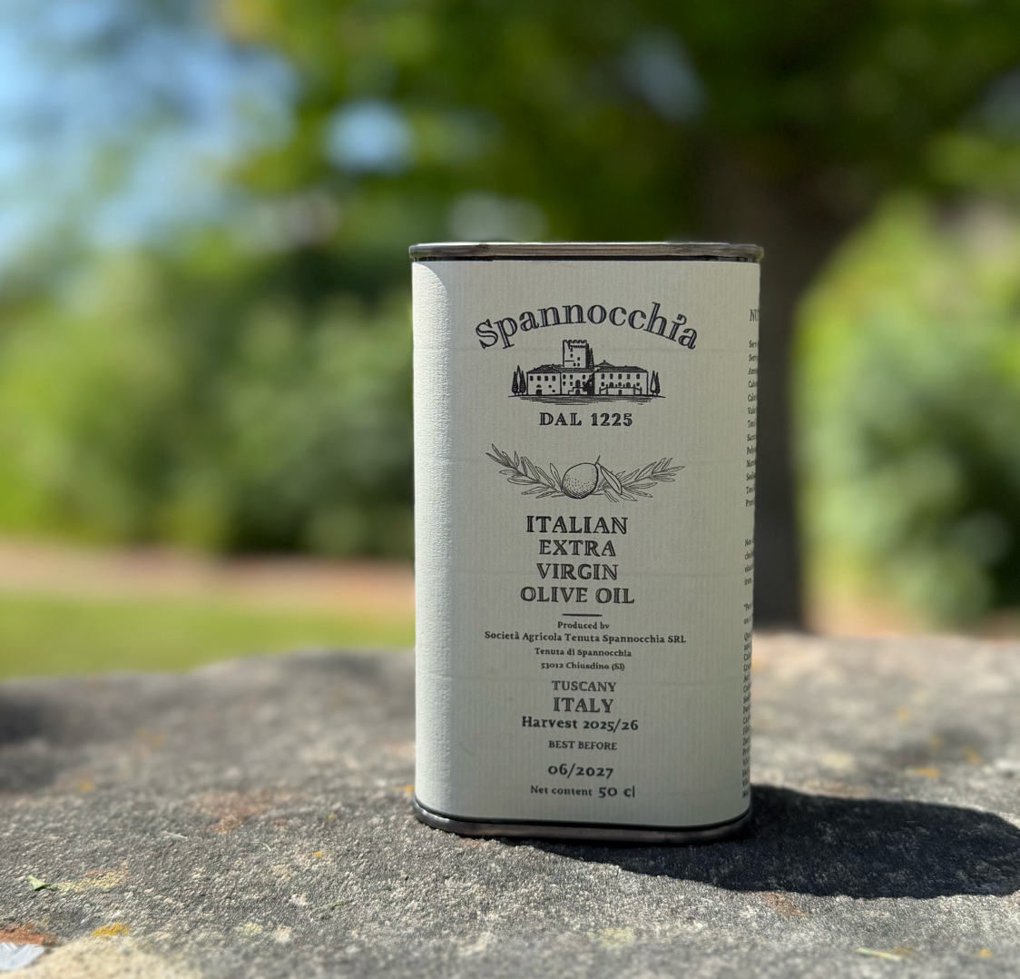 A 500ml can of Spannocchia olive oil standing on a rustic stone surface with blurred greenery in the background.