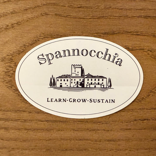 A vinyl sticker with the Spannocchia logo, placed on a wooden surface.