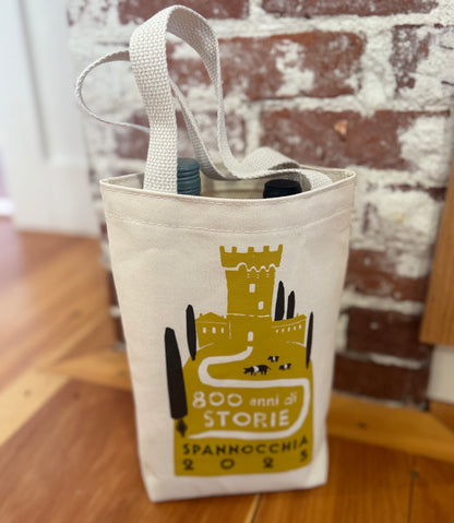 Tote bag with two wine bottle tops peeking out, against a rustic brick and wood background.