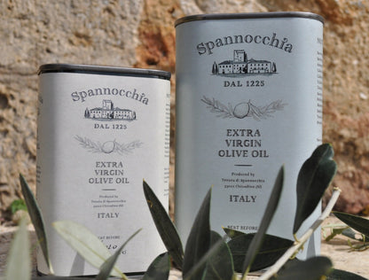 Two cans of Spannocchia olive oil with olive leaves in the foreground.