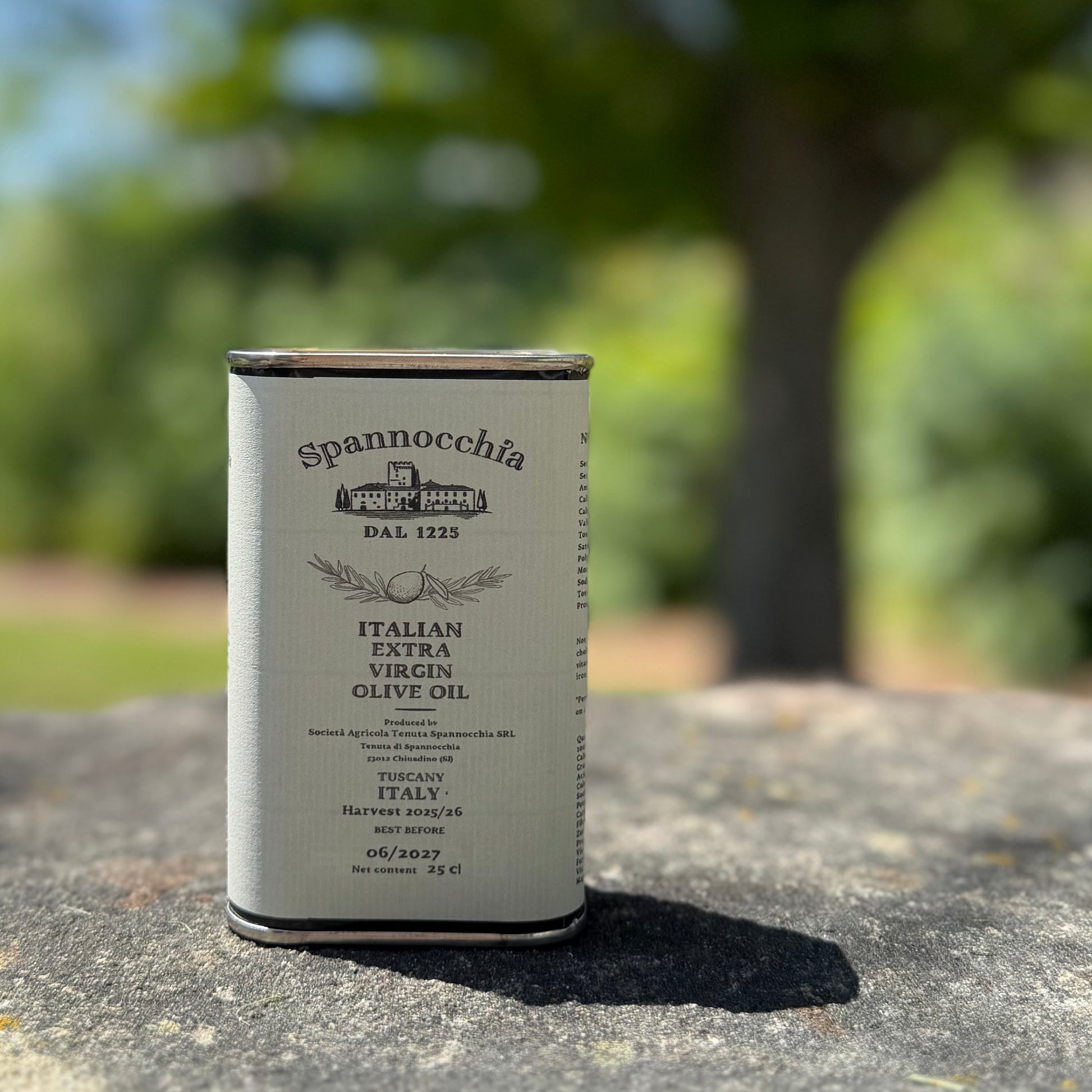 A 250ml can of Spannocchia olive oil standing on a rustic stone surface with blurred greenery in the background.