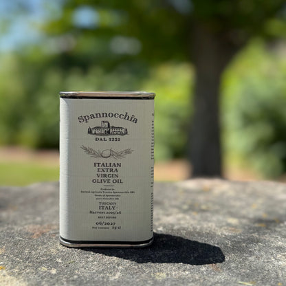 A 250ml can of Spannocchia olive oil standing on a rustic stone surface with blurred greenery in the background.