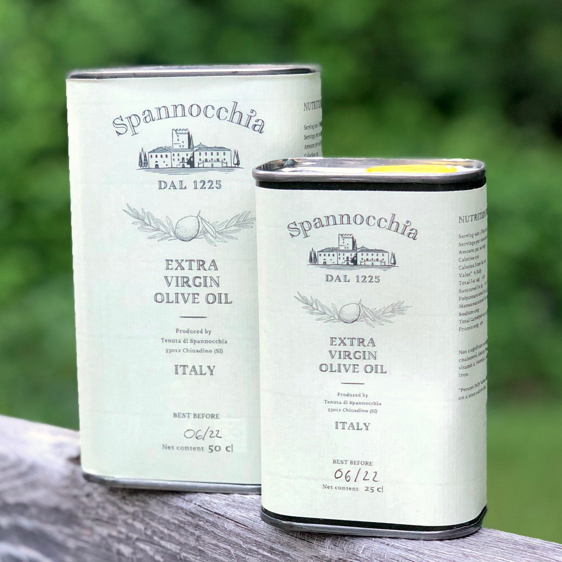 Two cans of Spannocchia olive oil with blurred foliage in the background.