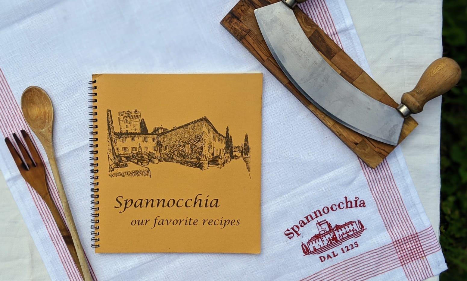 "Spannocchia, our favorite recipes" book cover, with mezzaluna, wooden utensils, and Spannocchia linen towel