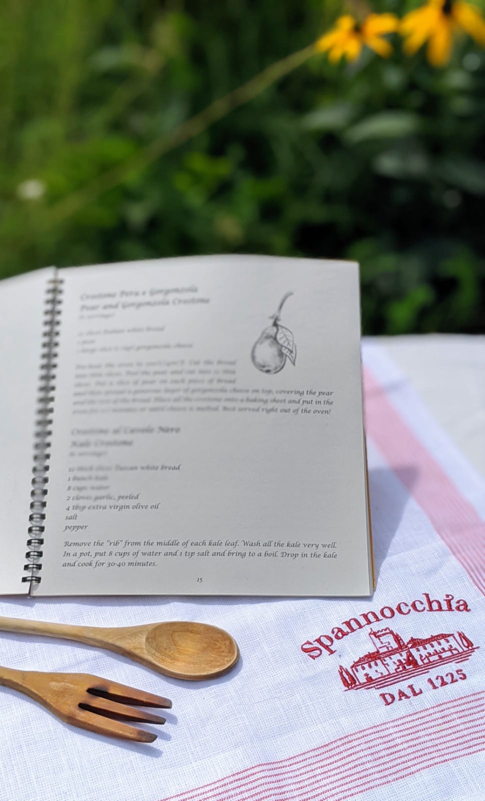 Open book showing a blurred recipe, with Spannochia linen towel and wooden utensils
