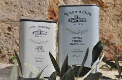 Two cans of Spannocchia olive oil with olive leaves in the foreground.